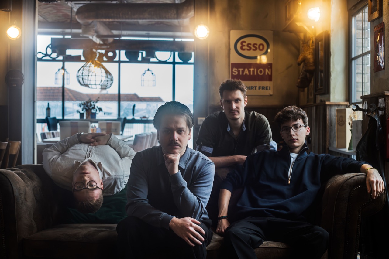 Die Mitglieder der Band sitzen in einem Club auf einer Ledercouch