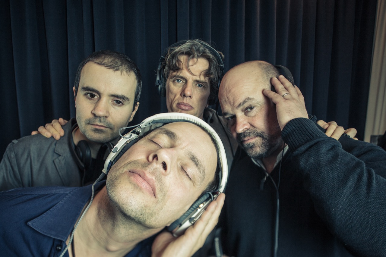 Joo Kraus und Tales in Tone<i></i>s Bandfoto: alle vier Köpfe der Band vor einem Bühnenvorhang, Joo im Vordergrund mit geschlossenen Augen Kopfhörer auf den Ohren und einer Kapuze darüber, in Musik versunken