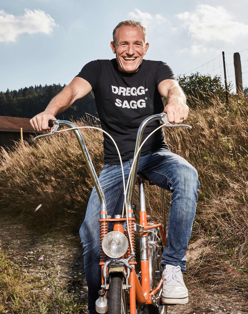 Michl Müller auf einem alten Klapp-/Bonanzarad | auf dem T-Shirt steht DREGG SAGG
