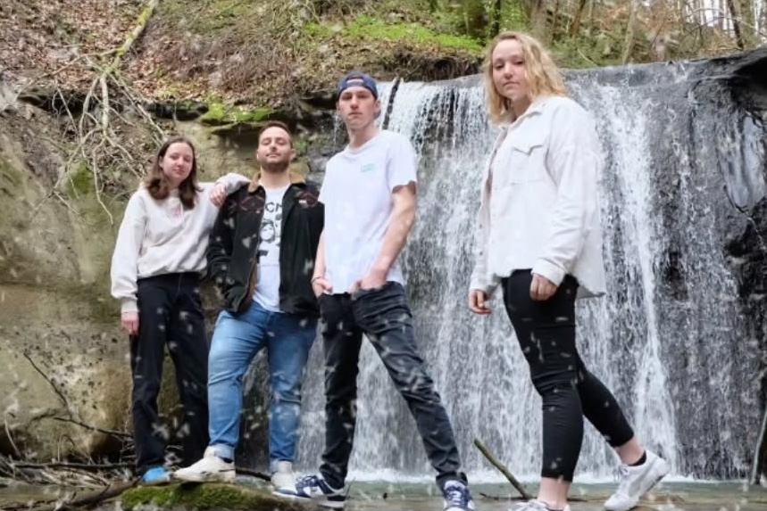 Bandmitglieder stehen im Wald vor einem Wasserfall
